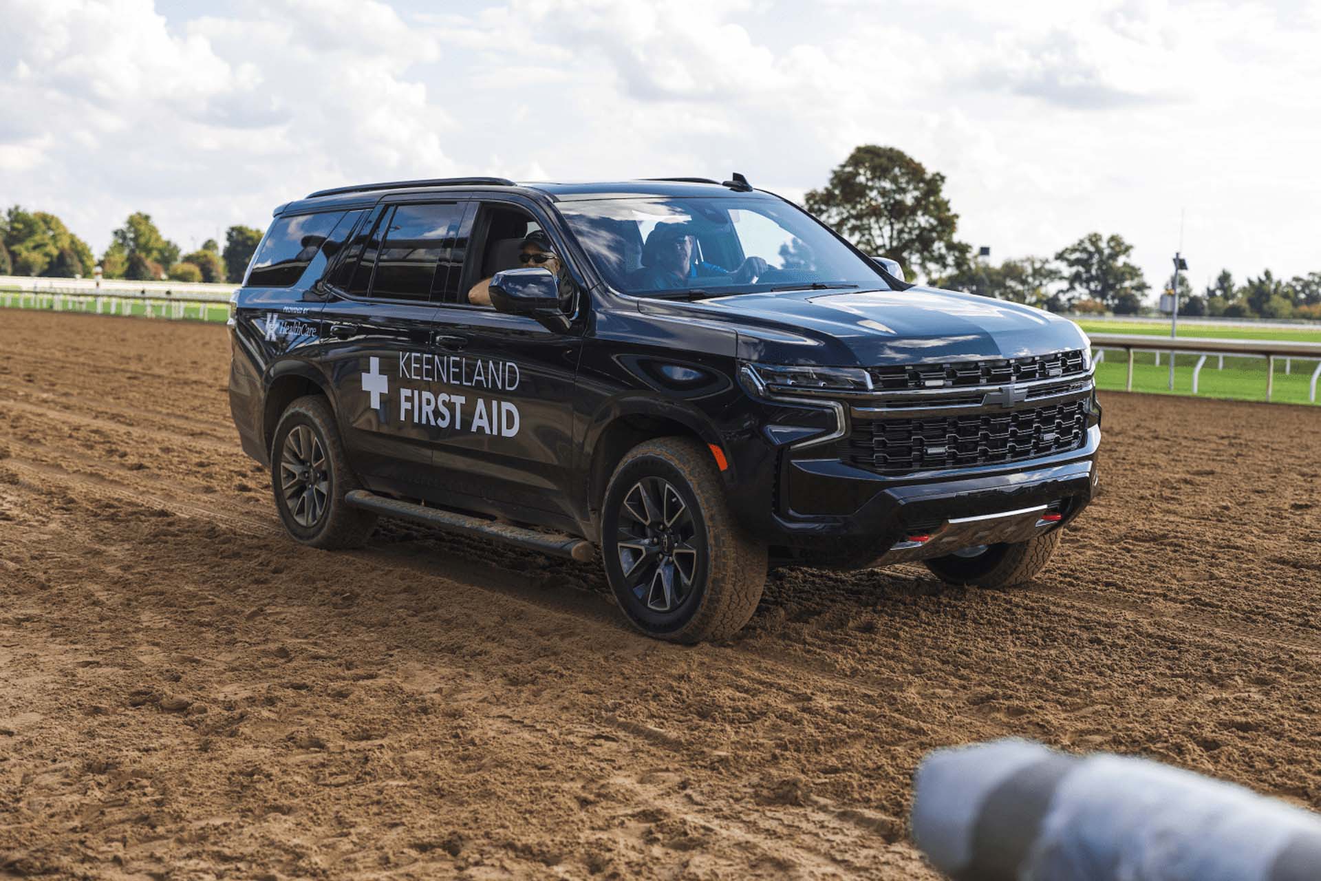 A picture of the Bestkeenland First Aid car on the dirt track. It is a large black Chevy SUV.